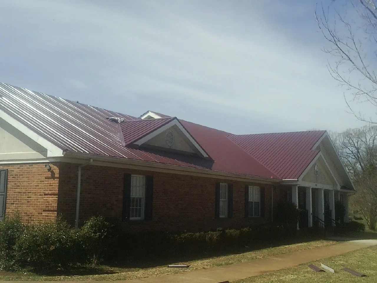 Red metal roof with gabled entries on a long brick building, from a Hail Damage Roof Repair job in Pitman